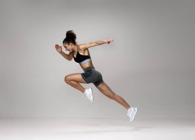 Sportif, genç ve güçlü bir kadının spor giyim eğitimindeki dinamik görüntüsü. Gri stüdyo geçmişine karşı yarışıyor. Spor yaşam tarzı, güzellik, vücut bakımı, fitness, sağlık, maraton kavramı