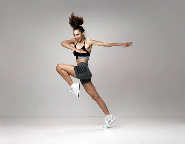 跳高年轻漂亮女子在运动服训练中的动态形象 在灰色工作室背景下摆姿势 运动生活方式 身体护理 健康的概念 — 图库照片