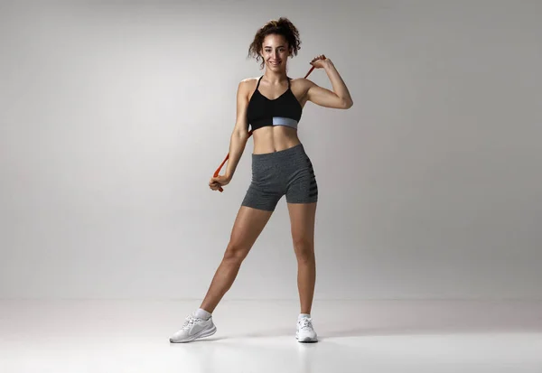 stock image Portrait of young girl in sportswear with musuclar body posing with fitness expanders against gray studio background. Concept of sportive lifestyle, beauty, body care, fitness, health