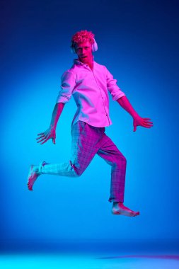 Kulaklıkla müzik dinleyen ve pembe neon ışıkta mavi stüdyonun arka planına atlayan olgun bir adamın tam boy portresi. İnsan duyguları kavramı, yaşam tarzı, gençlik, yüz ifadesi