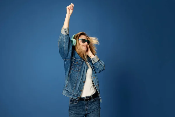 穿着牛仔裤的少女的画像 听着耳机里的音乐 在蓝色工作室的背景下跳舞 人类情感 面部表情 休闲的概念 — 图库照片