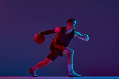 Genç atletik adam, topla hareket eden basketbolcu neon ışıkta mor stüdyonun arka planına karşı. Şampiyon. Profesyonel spor, hobi, sağlıklı yaşam tarzı, eylem ve hareket kavramı