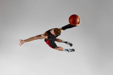 Kazanan gol. Sportif genç bir adam, hareketli bir basketbol oyuncusu, gri stüdyo arka planına karşı topla zıplıyor. Üst Manzara. Profesyonel spor, hobi, sağlıklı yaşam tarzı, eylem ve hareket kavramı