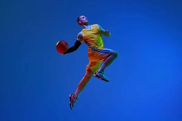 Junger Mann Basketballspieler Gelbem Uniformtraining Beim Ballwurf Vor Blauem Studiohintergrund — Stockfoto