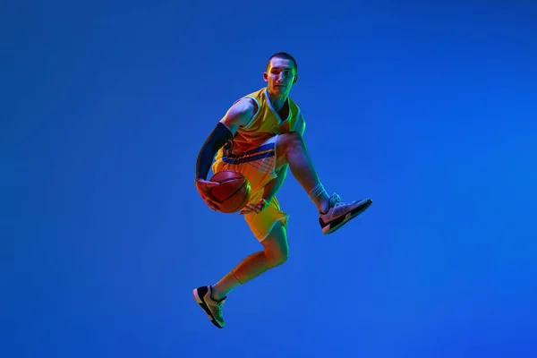 运动中的职业男篮运动员的动态形象 在霓虹灯背景下与蓝球一起跳跃 获胜的进球 职业体育 业余爱好 健康生活方式 行动的概念 — 图库照片