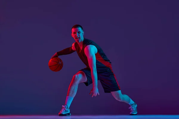 Junger Muskulöser Mann Basketballspieler Bewegung Dribbelnder Ball Vor Lila Studiohintergrund — Stockfoto