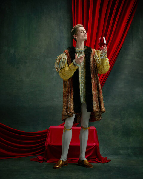 Portrait of young duke, prince, royal person in vintage costume raising glass of red wine against dark green, vintage background. Concept of comparison of eras, history, renaissance art, remake