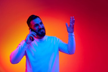 Sıradan giysiler içinde yakışıklı sakallı bir adamın portresi cep telefonuyla neon ışıklarıyla gradyan stüdyoda konuşuyor. Mutlu konuşmalar. İnsan duyguları, yüz ifadesi, yaşam tarzı kavramı
