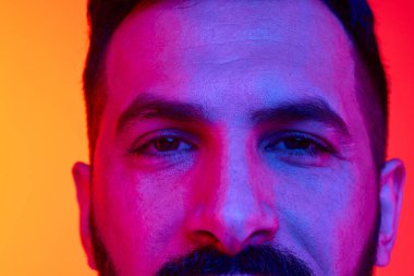 Yakın plan kırpılmış erkek gözleri, neon ışıklarındaki değişken kırmızı turuncu stüdyo arka planına karşı soğukkanlılıkla ve dikkatle bakıyor. İnsan duyguları, yüz ifadesi, yaşam tarzı kavramı