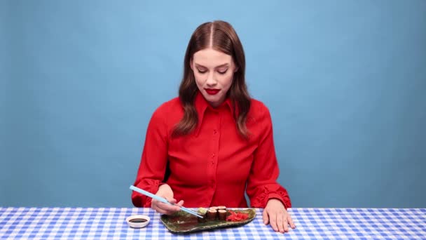 青いスタジオを背景に箸で辛いお寿司を食べる顔をした美しい若い女性 味の概念 人間の感情 顔の表情 — ストック動画