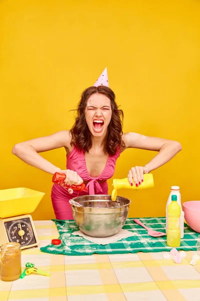 듯이보이는 감정적 소녀가 노란색 배경에 겨자와 케첩을 케이크를 만들고 있습니다 — 스톡 사진