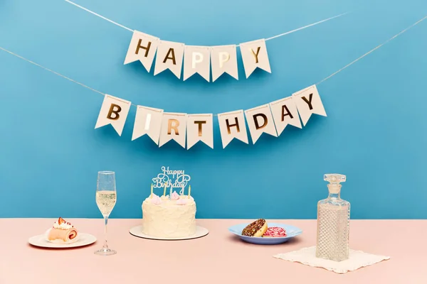 桌上有美味的蛋糕 香槟和蓝色背景的糖果 墙上装饰着快乐的生日信 准备的概念 流行艺术 — 图库照片