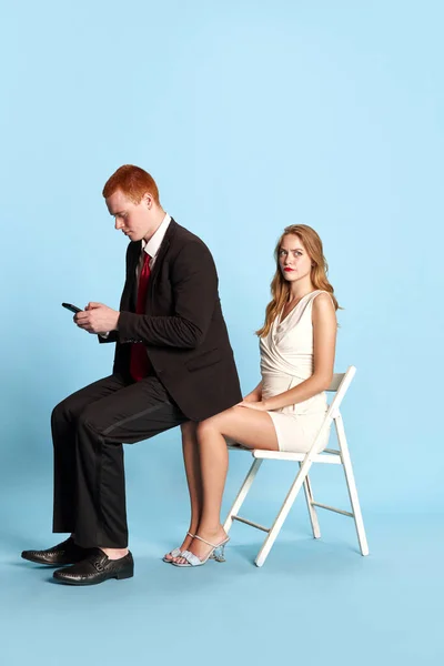年轻女人的脸很不愉快 年轻男人跪在她的膝盖上 在蓝色工作室背景下通过电话输入讯息 乐趣的概念 — 图库照片