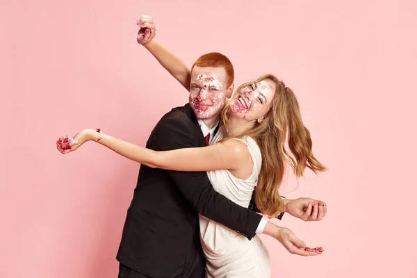 幸福的年轻夫妇的画像 男人和女人在庆祝婚姻 在粉红的工作室背景下吃着肮脏的蛋糕 乐趣的概念 — 图库照片