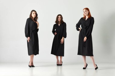 Üç stilin portresi, zarif siyah elbiseli güzel genç kadınlar ışık stüdyosunun arka planında poz veriyorlar. Zarif moda kavramı, kadın güzelliği, iş, alışveriş, satış, reklam