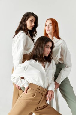 Güzel, zarif, şık kıyafetler, bluz ve pantolon giymiş genç kadınların portresi. Işık stüdyosu arka planında poz veriyorlar. Zarif moda kavramı, kadın güzelliği, iş, alışveriş, satış, reklam
