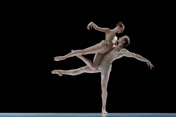 Support and love. Young talented man and woman, ballet dancers in beige bodysuits dancing against black studio background. Concept of beauty, classical dance style, inspiration, movements. Ad