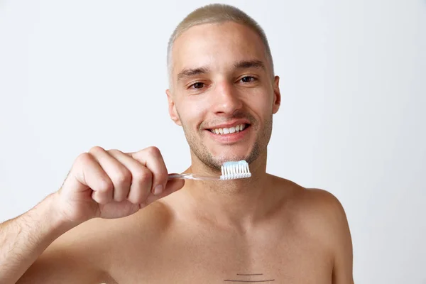 歯ブラシで無造作にポーズして白いスタジオの背景に貼り付ける完璧な白い歯を持つハンサムな若い男 男性の美しさ スキンケア 歯のケア 健康の概念 広告のコピースペース — ストック写真