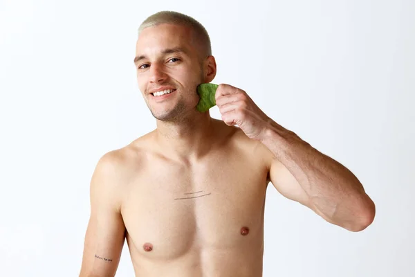 白いスタジオの背景に美容器具で顔マッサージをしている若いハンサムな男 顔を上げて 男性の美しさ スキンケア 健康の概念 広告のコピースペース — ストック写真