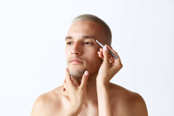 白いスタジオの背景に男の眉毛をプル女性の手 面倒見てくれるハンサムな若い男だ 男性の美しさ スキンケア 健康の概念 広告のコピースペース — ストック写真