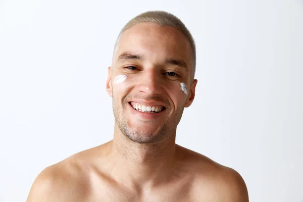 白いスタジオの背景に保湿クリームで肌の世話をする若い幸せな男の肖像画 男性の美しさ スキンケア 健康の概念 広告のコピースペース — ストック写真