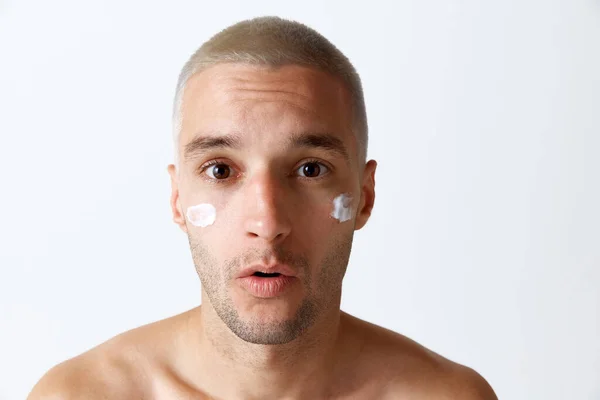 白いスタジオの背景に保湿クリームで肌の世話をする若いハンサムな男の肖像画 男性の美しさ スキンケア 健康の概念 広告のコピースペース — ストック写真