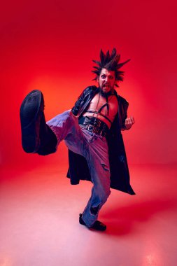 Olağanüstü giysiler içinde duygusal genç bir punk, makyaj malzemeleri ile kırmızı stüdyo arka planına karşı illüzyon gitar çalıyor. Müzik, yaşam tarzı, alt kültür, sanat, gençlik, insan duyguları kavramı