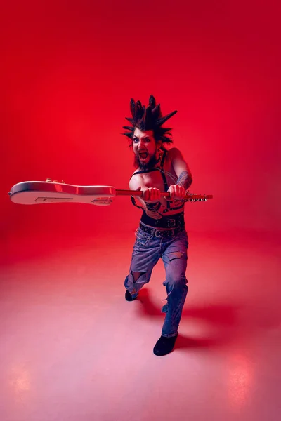 疯狂的庞克情绪化的年轻人 摇滚音乐人在霓虹灯下 用电吉他对着红录音棚的背景摆出咄咄逼人的姿势 生活方式 亚文化 人类情感的概念 — 图库照片