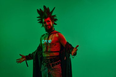 Etkileyici genç adam, rock müzisyeni, vücudunda neon filtresi olan punk neon ışıkta yeşil stüdyo arka planına karşı poz veriyor. - Doğru. Müzik, yaşam tarzı, alt kültür, sanat, gençlik, insan duyguları kavramı