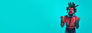 Gömleksiz genç adam, çılgın saçlı ve makyajlı serseri mavi stüdyo arka planında neon ışıkta poz veriyor. Müzik anlayışı, yaşam tarzı, alt kültür, sanat, gençlik, insan duyguları. Pankart. İlan için alanı kopyala