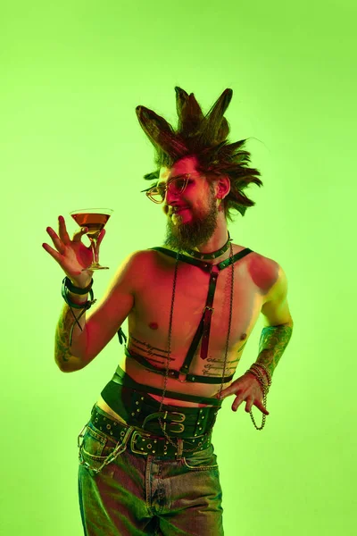 派对时间年轻的无上衣男子 双关语在非凡的发型喝鸡尾酒 在霓虹灯下的绿色工作室背景上摆姿势 生活方式 亚文化 人类情感的概念 — 图库照片