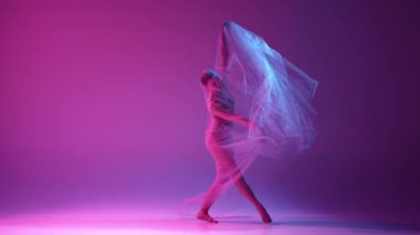 Şefkatli, yetenekli genç bir kız, bej renkli bir balerin şeffaf duvağıyla neon ışıkta pembe renkli stüdyo arkaplanının üzerinde dans ediyor. Klasik sanat kavramı, dans, güzellik, ilham