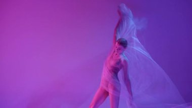 Özgürlük için. Şeffaf kumaşla dans eden genç ve narin bir balerin neon ışıklarıyla mor renkli bir stüdyo stüdyosuna karşı. Klasik sanat, dans, güzellik, ilham, yaratıcılık kavramı