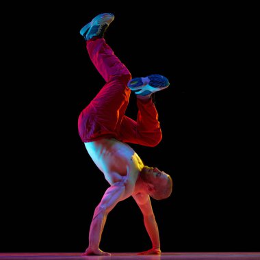 Genç, yetenekli, kaslı vücut dansı yapan, hip-hop 'la neon ışıkta siyah stüdyonun arka planına karşı. Sanat kavramı, sokak dansı, moda, gençlik, hobi, dinamik, reklam