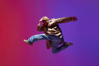 Şık kıyafetler içinde dans eden, pembe mor stüdyo arka planına karşı hip-hop yapan yetenekli genç adamın dinamik görüntüsü. Sanat kavramı, sokak dansı, moda, gençlik, hobi, dinamik, reklam