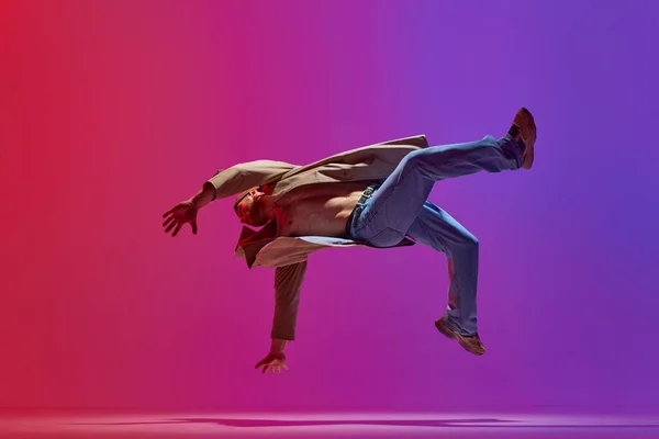 stock image Dance show. Young guy in stylish clothes dancing hip hop, breakdance, contemp against pink purple studio background. Concept of art, street style dance, fashion, youth, hobby, dynamics, ad