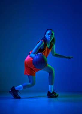 Kazanmak için motivasyon. Genç bayan basketbolcu oyun sırasında neon ışıklarıyla mavi stüdyonun arka planına karşı hareket ediyor. Profesyonel spor, eylem ve hareket kavramı, oyun, rekabet, hobi, reklam