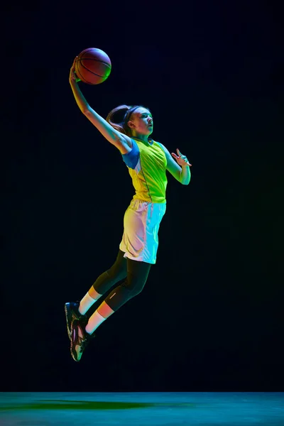 スラムダンク 動きの女性バスケットボール選手 ネオンで黒のスタジオの背景にボールでジャンプ プロスポーツ アクションと運動 ゲーム 広告の概念 — ストック写真