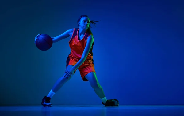 若い女の子のダイナミックなイメージ 動きの中で均一なバスケットボール選手 ネオンの光の中で青のスタジオの背景で遊んでいます プロスポーツ アクションと運動 ゲーム 広告の概念 — ストック写真