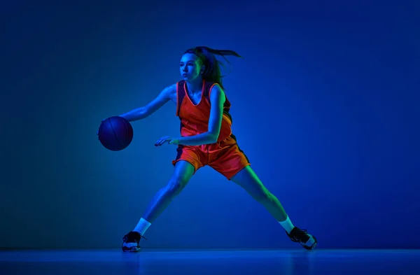 女性バスケットボール選手のトレーニング ネオンで青のスタジオの背景にドリブルボールを集中 プロスポーツ アクションと運動 ゲーム 広告の概念 — ストック写真