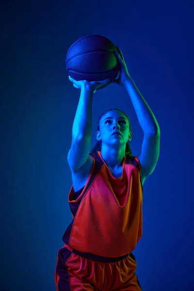 获胜的进球 年轻姑娘 全神贯注的篮球运动员在霓虹灯下在蓝色工作室的背景下投球 职业运动 动作和运动 业余爱好 广告的概念 — 图库照片