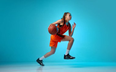 Genç atletik kız, hareketli basketbol oyuncusu, neon ışıkta mavi stüdyo arka planında topla koşuyor. Profesyonel spor, eylem ve hareket kavramı, oyun, rekabet, hobi, reklam