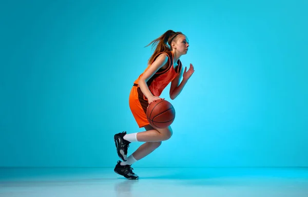 年轻的女孩 运动中的篮球运动员 在霓虹灯下与蓝色工作室背景的球赛跑 职业运动 动作和运动 业余爱好 广告的概念 — 图库照片
