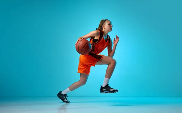年轻的女运动员 运动中的篮球运动员 带着球在霓虹灯下与蓝色工作室背景赛跑 职业运动 动作和运动 业余爱好 广告的概念 — 图库照片