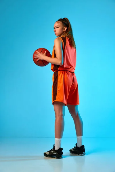 侧视图全长的少女形象 身穿制服的篮球运动员在霓虹灯下与蓝色工作室背景的球对齐 职业运动 动作和运动 业余爱好 广告的概念 — 图库照片