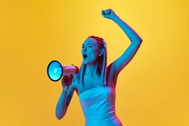 Sosyal hareketler. Duygusal olarak zıplayan genç bir kızın portresi ve neon ışıkta sarı stüdyonun arka planına karşı duygusal olarak bağıran bir megafon. Gençlik kavramı, duygular, güzellik, yaşam tarzı, reklam