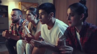 Gençler, evdeki kanepede oturan arkadaşlar ve televizyonda futbol maçı izleyen taraftarlar favori takımı neşelendiriyor. Başarılı bir oyun. Boş zaman kavramı, spor hayranları, dostluk, duygular.