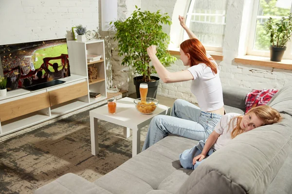 Stock image Young woman sitting on couch at home and attentively watching football match on tv. Little girl, child feeling bored and sleepy. Concept of hobby, entertainment, lifestyle, sport, leisure, emotions