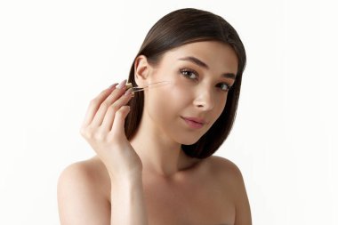 Güzel, cilt bakımını organik kozmetiklerle, yüz serumuyla, beyaz stüdyo arka planında nemlendirici ile yapan genç bir kadın. Kadın güzelliği, vücut ve cilt bakımı, kozmetoloji, sağlık, reklam