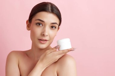 Pembe stüdyo arka planında yüzü nemlendirici kremle poz veren güzel bir kadının portresi. Deri hidrasyonu. Doğal kadın güzelliği kavramı, vücut ve cilt bakımı, kozmetoloji, sağlık, reklam